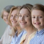 Close up faces in row, diverse women smile looking at camera, little cute girl, her adult mother, mature grandmother and old great-grandmother portraits. Multi-generational family, heredity, offspring