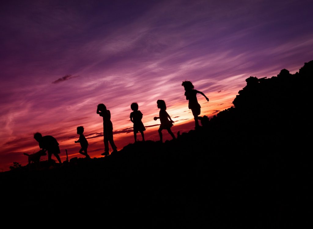 Six children walking in a row with a sunset behind them.