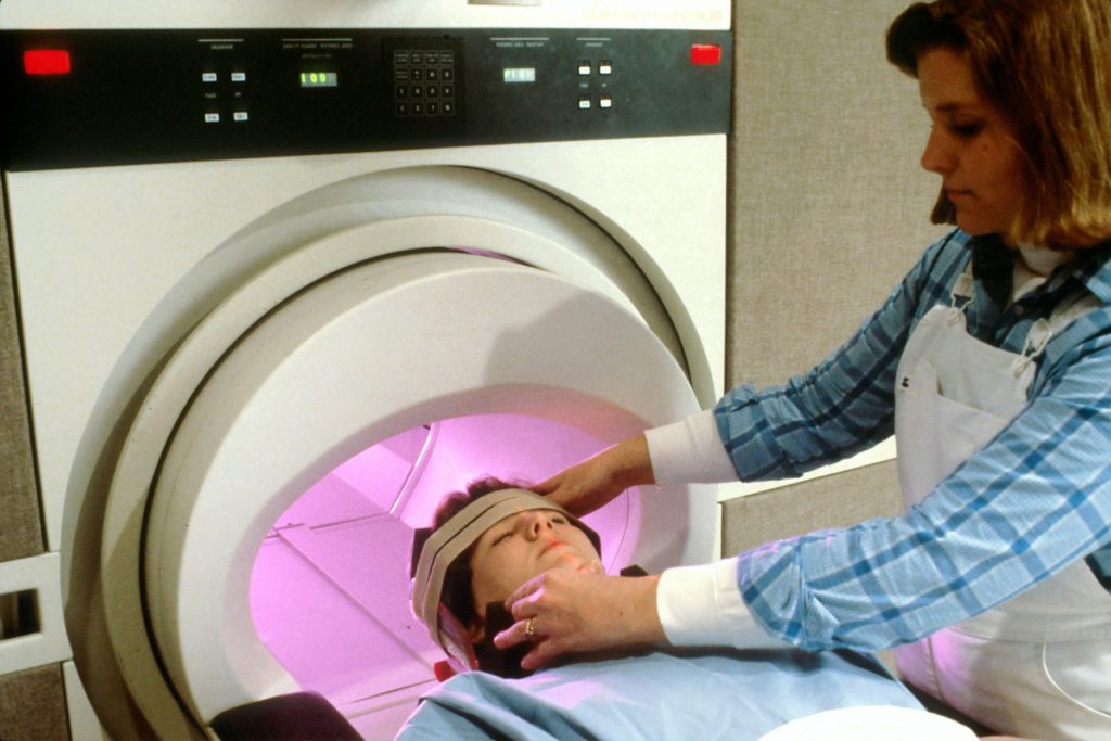 Someone entering an MRI scanner with a clinician angling their head in the correct position. 