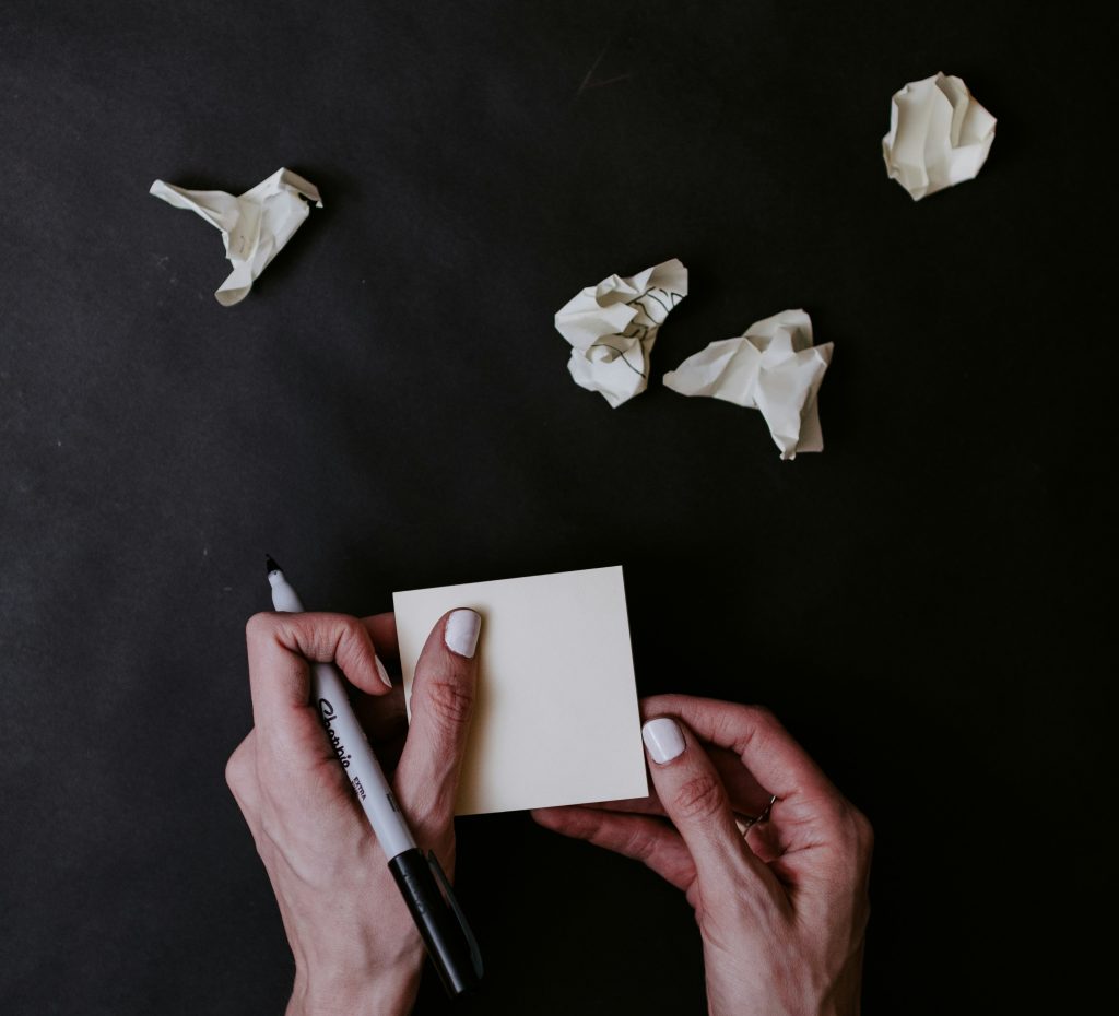 Person writing on blank paper with screwed up paper around them