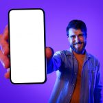 Cheerful,Guy,Holds,Large,Smartphone,Showing,Empty,Device,Screen,,Offering