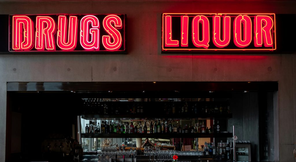 Picture of a bar with the words drugs and liquor in lights above the bar.