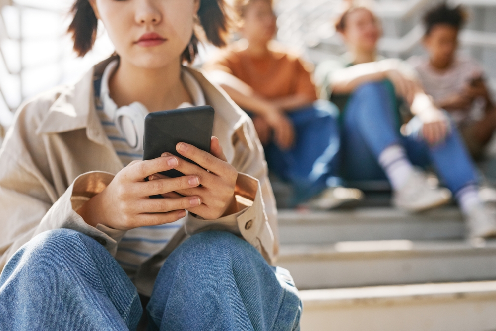 Closeup,Of,Teenage,Girl,Holding,Smartphone,Outdoors,While,Sitting,On