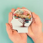 Hands holding paper head, human brain with flowers, self care and mental health concept, positive thinking, creative mind