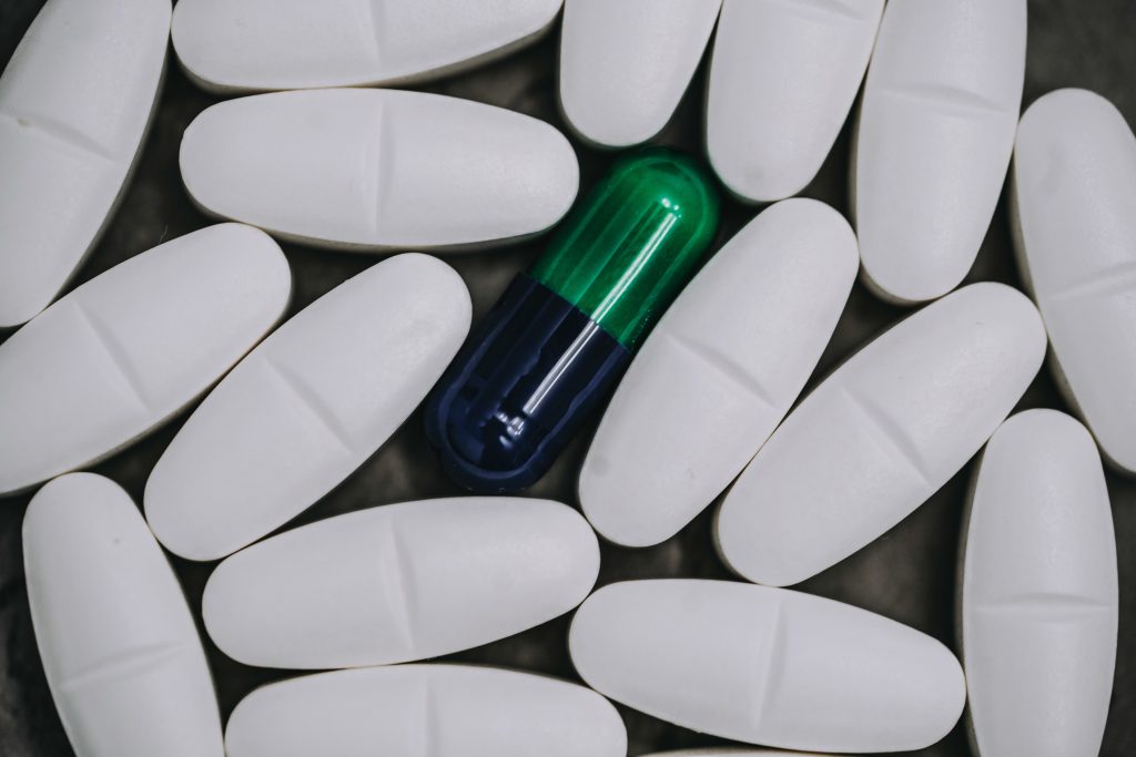 One pill capsule sits within a group of white hard pills