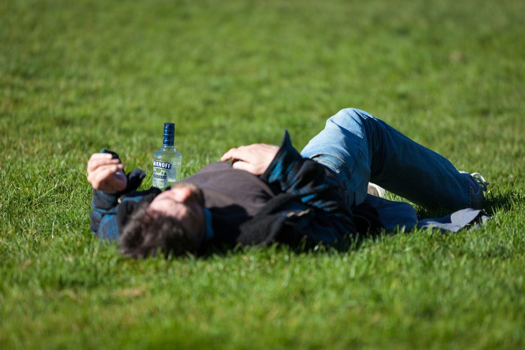 a man laying in the grass with a bottle of vodka