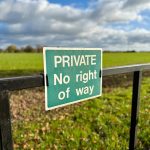 A sign on a gate showing the way forward is no right of way and private land with a blue sky above